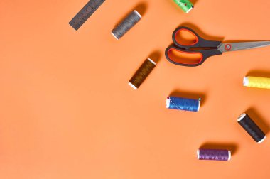 Aksesuar makası, metal cetvel, atölyedeki turuncu terzi masasına renkli iplikler ve iğneler dikmek. Mesaj için yer var. Üst yaşam