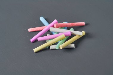 Siyah karatahtanın üzerinde bir sürü renkli tebeşir parçası. Yakın plan.