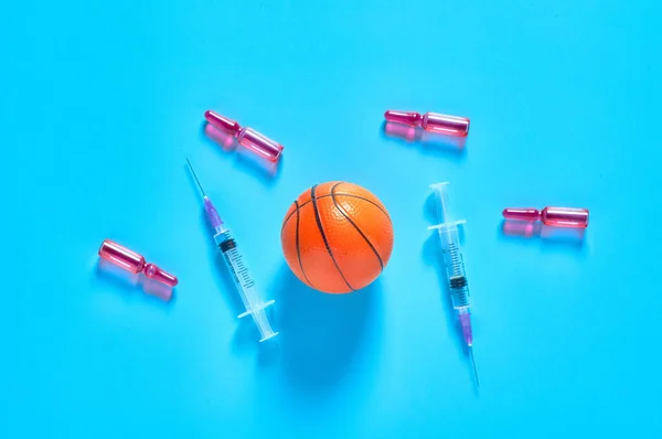 Basketball ball near syringe and ampoule on blue background. Concept of doping in professional sport. Rehabilitation, treatment after competition. Illegal medicaments using on tournament