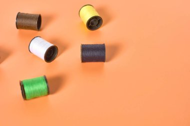 Atölyedeki turuncu terzilerin masasına renkli ipliklerle saçılmış makaralar. Metin için boşluk