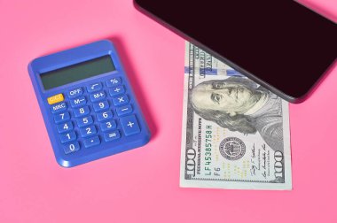 Akıllı telefon, hesap makinesi ve pembe arka planda dolar banknotu. Mobil bankacılık kavramı. Evden online alışveriş. Uzaklık denetimi mali denge