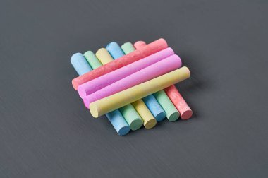 Siyah karatahtanın üzerinde bir sürü renkli tebeşir parçası. Yakın plan.