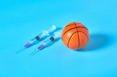 Mavi arka planda şırınganın yanında basketbol topu. Profesyonel sporda doping kavramı. Rehabilitasyon, yarışmadan sonra tedavi. Turnuvada kullanılan yasadışı ilaçlar