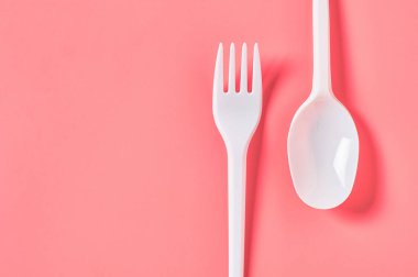 Pembe arka planda tek kullanımlık beyaz kaşık ve çatal. Çevreyi, ekolojiyi, piknik, parti ve diğer etkinlikleri kurtarma kavramı. Üst Manzara. Boşluğu kopyala