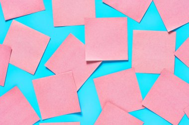 Mavi arka planda bir sürü pembe kare boş kağıt çıkartması vardı. Uzayı kopyala Üst görünüm