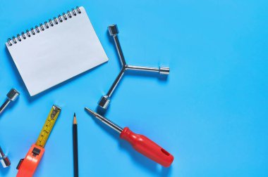 Farklı araçlar atölyedeki mavi masadaki boş kağıt defterin yanında yatıyor. Mesaj için yer var. Üst görünüm