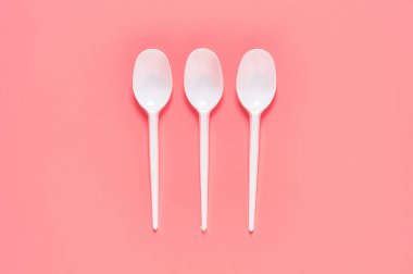 Pembe arka plana saçılmış tek kullanımlık beyaz kaşıklar. Çevreyi, ekolojiyi, piknik, parti ve diğer etkinlikleri kurtarma kavramı. Üst görünüm