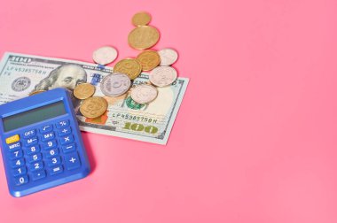 100 dolarlık banknot ve pembe arka planda hesap makinesinin yanında farklı paralar.