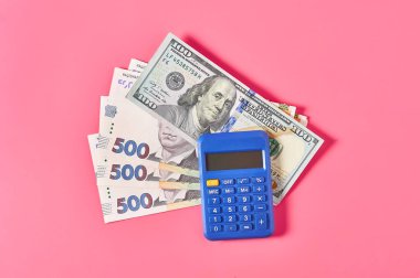 100 dolarlık banknot ve hesap makinesinin yanındaki Ukrayna parası pembe arka planda.
