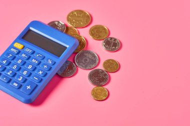 Pembe arka planda hesap makinesinin yanında farklı metal paralar