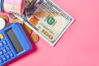 100 dolarlık banknot ve hesap makinesinin yanındaki Ukrayna parası pembe arka planda.