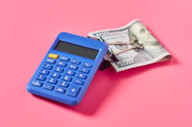 Pembe arka planda, hesap makinesinin yanında 100 dolarlık banknot.