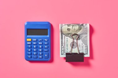 Pembe arka planda, hesap makinesinin yanında 100 dolarlık banknot.