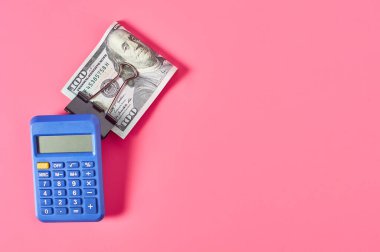 Pembe arka planda, hesap makinesinin yanında 100 dolarlık banknot.