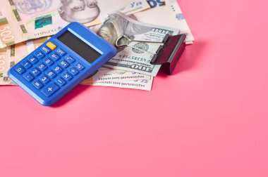 100 dolarlık banknot ve hesap makinesinin yanındaki Ukrayna parası pembe arka planda.