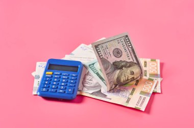 100 dolarlık banknot ve hesap makinesinin yanındaki Ukrayna parası pembe arka planda.