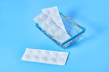 Beyaz ambalaj, mavi arka planda market sepetinde haplar. İlaç almak ya da satmak. Sağlık hizmetleri kavramı