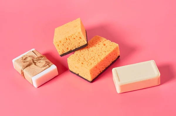 Scattered bricks of soap in vintage packing near sponges on pink background. Hygiene and cleaning concept