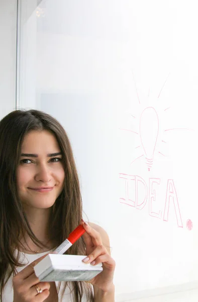 Cute girl smiling drew Idea with a red marker on a window