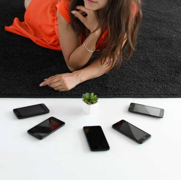 Close up of a girl in orange dress with 5 phones and succulent plant
