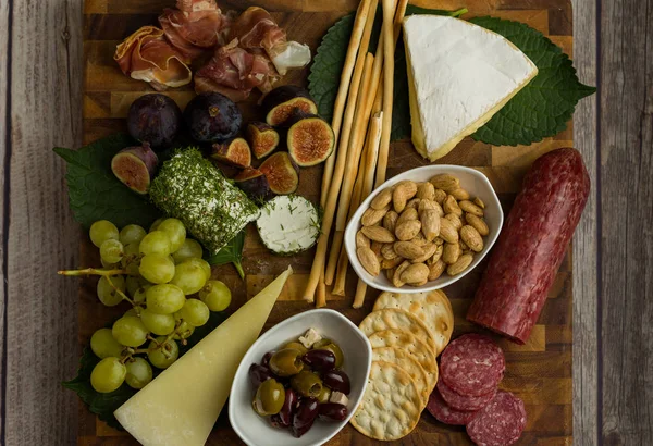 Cheese board flat lay shot with cheese, bread sticks, crackers, figs, grapes, goat cheese, brie cheese, almonds, nuts, and olives