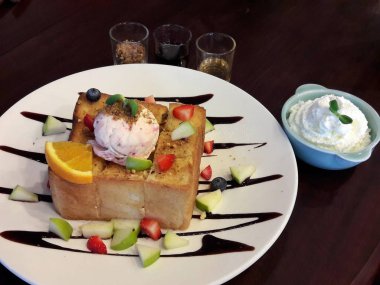 çilek, elma, portakal ve yaban mersini küçük parçalar bir kaşık dondurma üstünde belgili tanımlık tepe ve küçük bir kase krem şanti ile süslenmiş beyaz plaka tatlı bal tost