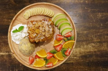 Tatlım meyveli tost ekmeği bir tabak dondurma bir kepçe ile süsleyin, kamçı krema, muz, portakal, çilek, elma, kivi meyve ve Mısır pul. Kahverengi ahşap masanın üzerinde                  