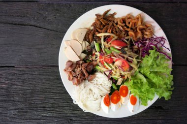 Tay papaya salatası veya Som Tum ahşap masada yumurta, sebze, kurutulmuş balık, yerel erişte gibi bazı yan yemekler ile dekore beyaz tabakta