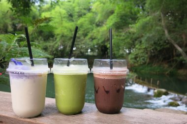 içecek üç bardak - buzlu kakao, yeşil çay ve frappe hindistan cevizi suyu taze doğa atmosferinde ahşap masaya yerleştirerek ağaçlar ve biraz dere ile çevrili