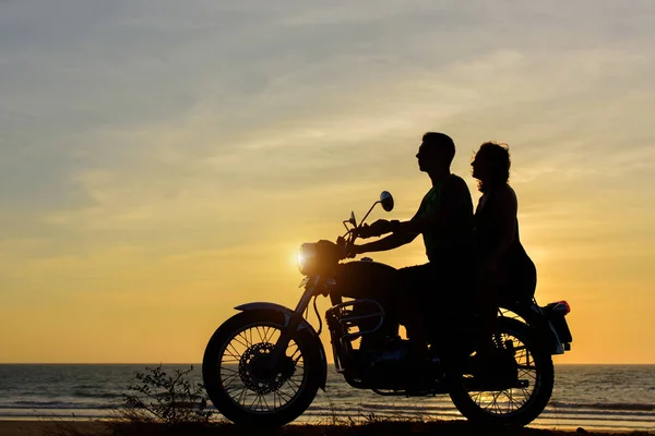 Silhouettes of guy and girl on motorcycle on sunset background. Young couple are sitting on motorcycle, faces in profile.