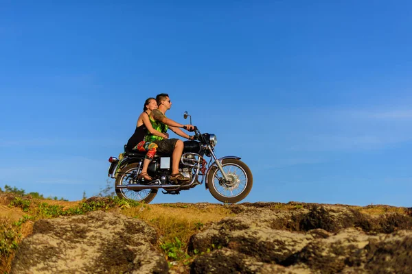 Young couple on a motorcycle on on rocky ground. Happy guy and girl travelling on a motorbike.