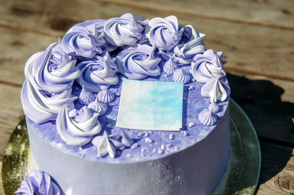 Purple birthday cake with cream flowers on wooden background, close up. Wedding sweets, blueberry cake decorated with decorative sticker, top view.