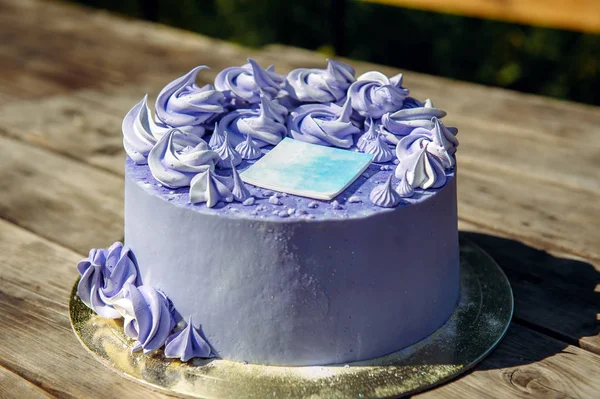 Purple birthday cake with cream flowers on wooden background, close up. Wedding sweets, blueberry cake decorated with decorative sticker, top view.