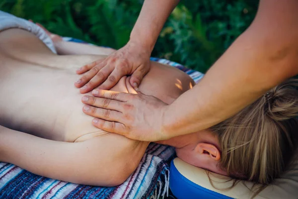 Hands masseur on the back of patient close-up. Woman on massage treatments at the Spa outdoor. Relaxed woman receiving wellness massage. Manual therapy, restoration of health of the back and spine.