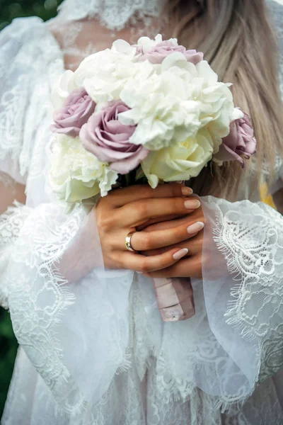 Hands of young bride holding beautiful wedding bouquet. Bride\'s hand with a wedding ring on her finger. Bride in vintage white dress holds a bouquet of roses.