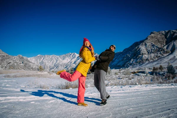 Young loving happy couple embraces and enjoys a new year vacation in the mountains. Guy and girl holding hands on the background of snow-capped mountains. Christmas holidays and travel.