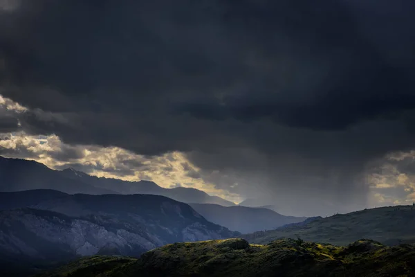 Dramatic dark clouds in mountains before storm. Landscape with mountain range, rain clouds and rays from the sun. Epic natural background.
