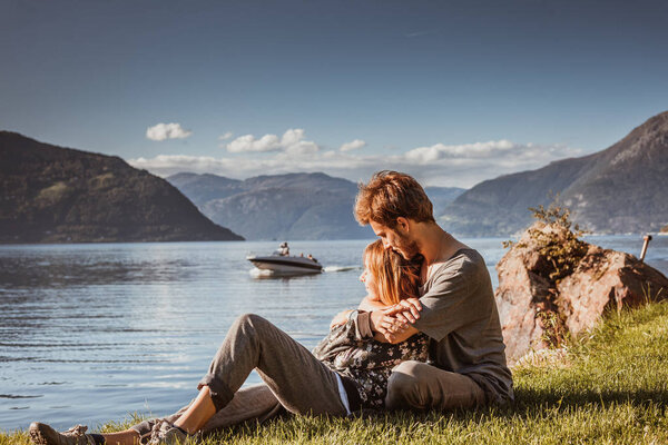 picturesque view of couple in love hugging while sitting by lake in mountains, Norway