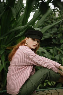 zemin üzerine yeşil bitkiler ile oturan siyah kap ve pembe çizgili gömlek şık genç kadın 
