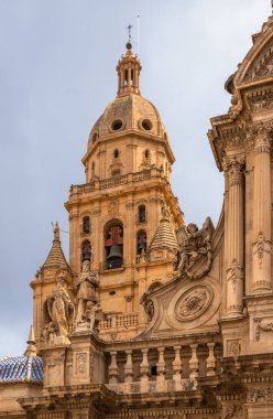 İspanya 'daki Murcia Katedrali' nin çarpıcı cephesi. Karmaşık Barok mimarisi, detaylı heykeller ve bulutlu bir gökyüzü altında tarihi cazibe sergileniyor.