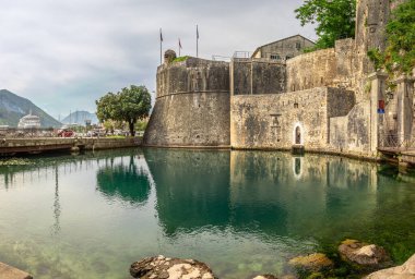 Karadağ 'ın Kotor kentindeki tarihi kale duvarları, arka planda dağlarla birlikte sakin sulara yansıyor. İkonik UNESCO Dünya Mirası