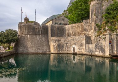 Karadağ 'ın Kotor kentindeki tarihi kale duvarları, arka planda dağlarla birlikte sakin sulara yansıyor. İkonik UNESCO Dünya Mirası