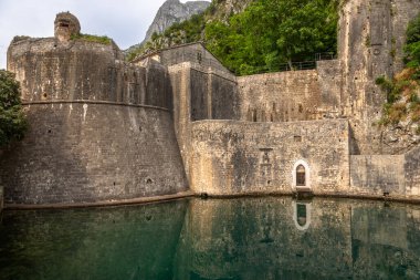 Karadağ 'ın Kotor kentindeki tarihi kale duvarları, arka planda dağlarla birlikte sakin sulara yansıyor. İkonik UNESCO Dünya Mirası