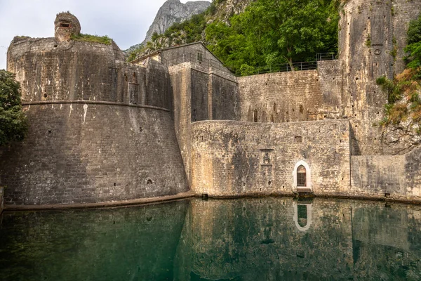 Karadağ 'ın Kotor kentindeki tarihi kale duvarları, arka planda dağlarla birlikte sakin sulara yansıyor. İkonik UNESCO Dünya Mirası