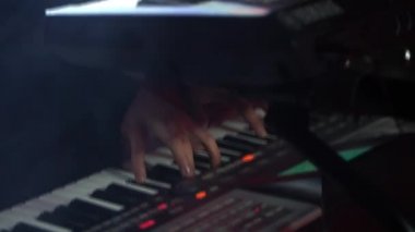 Genç yakışıklı bir adam, arka planda yanıp sönen kırmızı ampuller ve dumanlı bir sentezleyiciyle oynar.