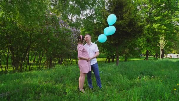 Un hombre con una mujer embarazada parada en el parque con globos azules — Vídeos de Stock