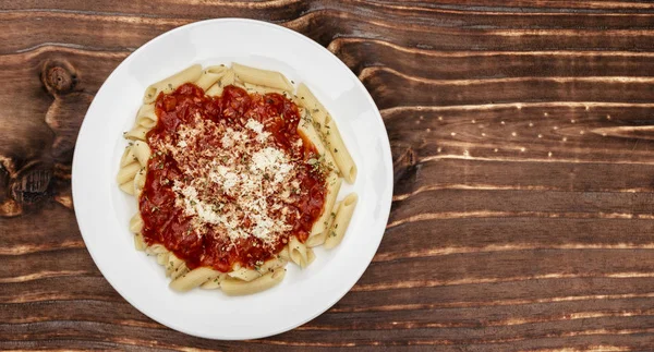 penne meal with red sauce and grated cheese, wooden background, top view