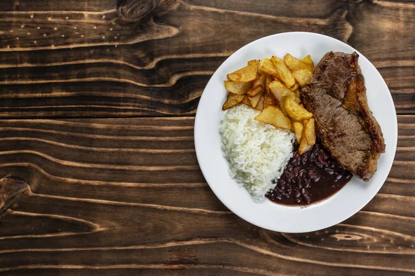 Beyaz plaka üzerinde yemek, pirinç, fasulye, biftek ve cips, ahşap arka plan