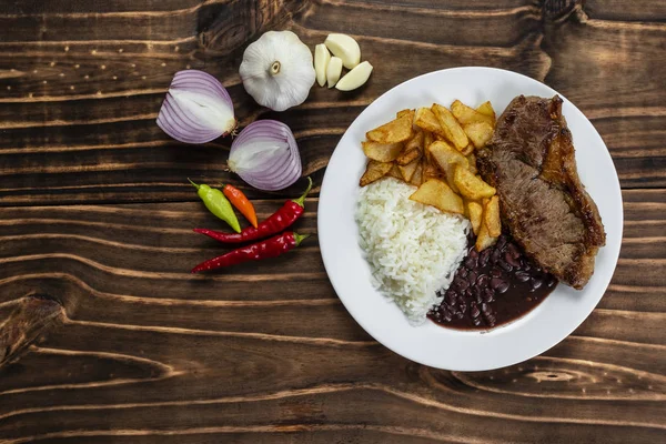Beyaz plaka üzerinde yemek, pirinç, fasulye, biftek ve cips, ahşap arka plan