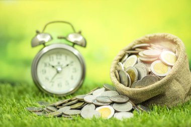 Zaman para kavramı, çim çanta ve çalar saat arka planda çok madeni para kaydetmek için